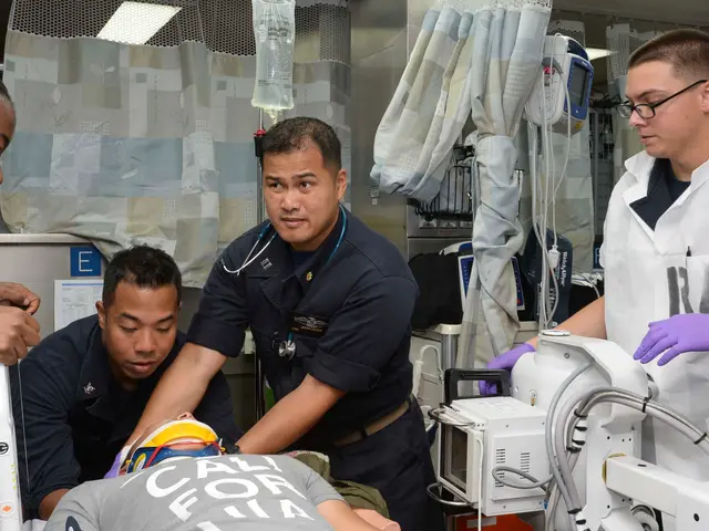 The image shows a group of four people standing around a man laying on a gurney in a hospital room....