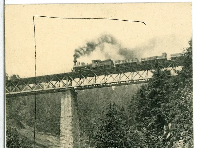 The image shows an old black and white photo of a train crossing a bridge, with smoke billowing...