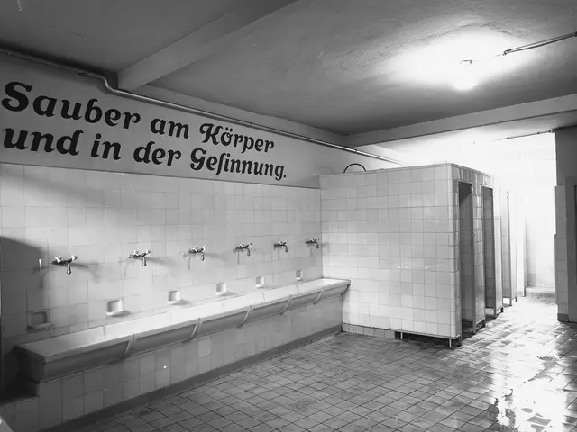 The image shows a black and white photo of a public restroom with a tiled floor, a wall with text...