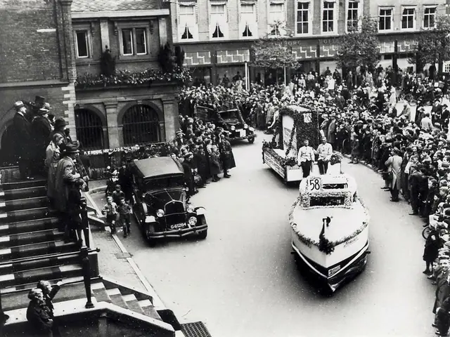 The image shows a black and white photo of a crowd of people watching a parade on a city street....