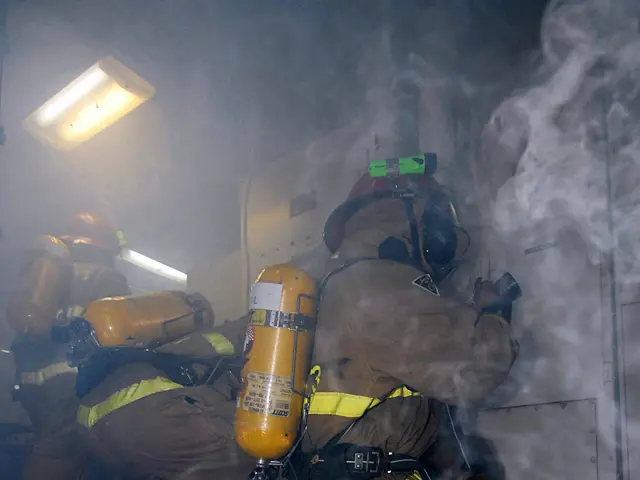 The image shows a group of firefighters in a room with smoke coming out of a door, wearing helmets...