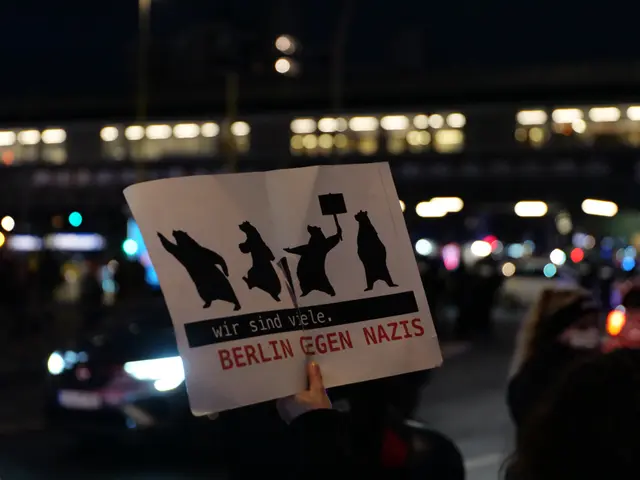 The image shows a person holding up a sign that reads "Berlin Gegen Nazis" in front of a crowd of...
