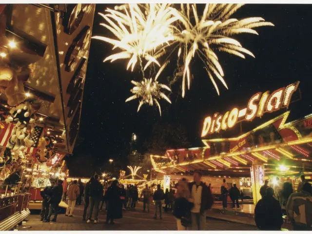 The image shows a crowd of people standing in front of a carnival ride at night, illuminated by...