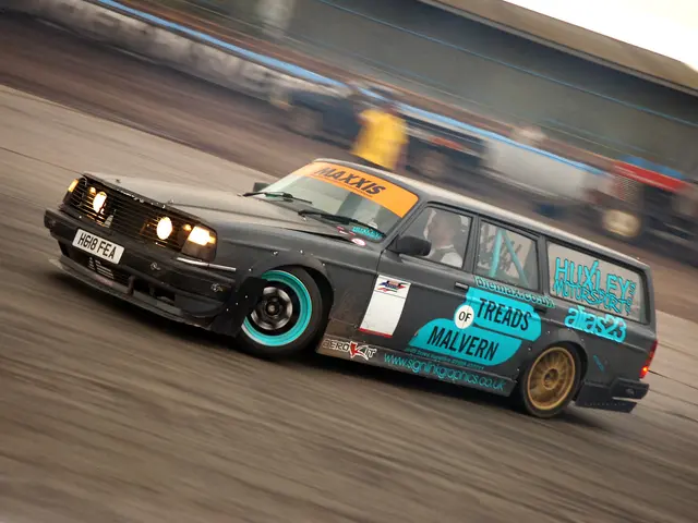 The image shows a car driving down a race track with a person inside, surrounded by other vehicles....