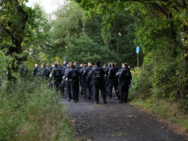 The image shows a group of police officers walking down a dirt road surrounded by trees and plants...