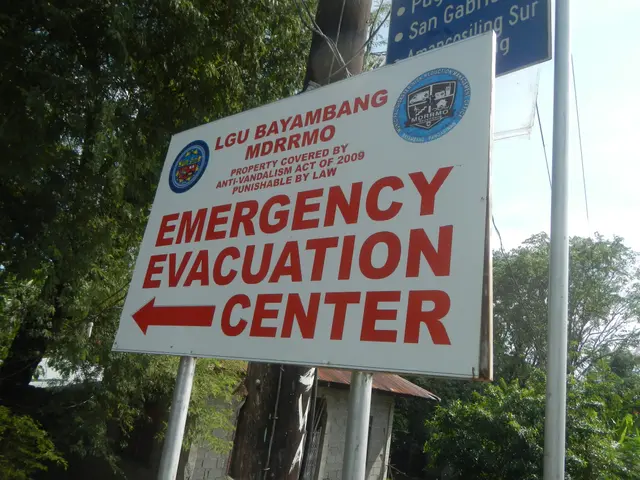 The image shows an emergency evacuation center sign on the side of a road, surrounded by trees and...