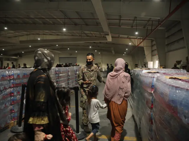 The image shows a group of people walking through a warehouse filled with water bottles,...
