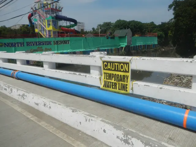 The image shows a bridge with a caution sign on it that reads "Caution Temporary Water Line". There...