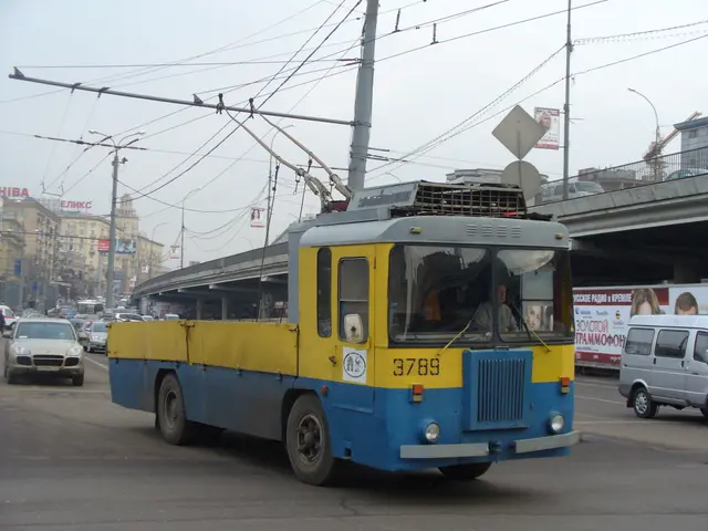 The image shows a blue and yellow trolleybus driving down a city street, surrounded by other...