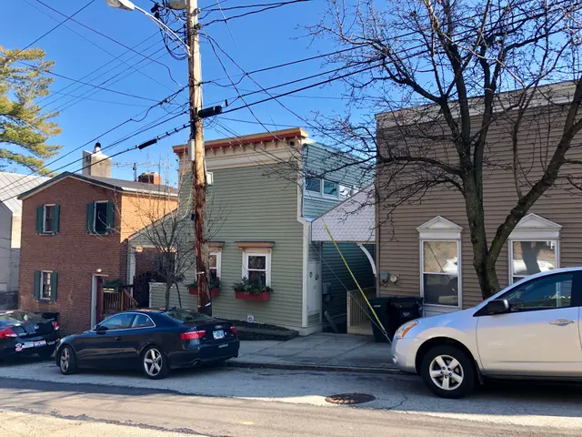 The image shows a street with cars parked on the side of it, a pole with wires, a light pole,...