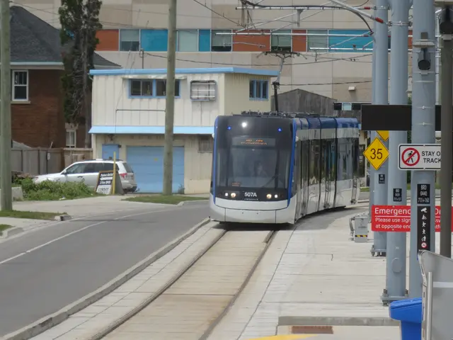 The image shows a light rail train traveling down a street lined with tall buildings. On the right...