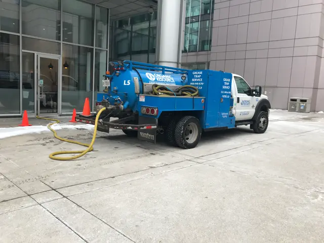 The image shows a blue and white truck parked in front of a building with glass walls and doors....