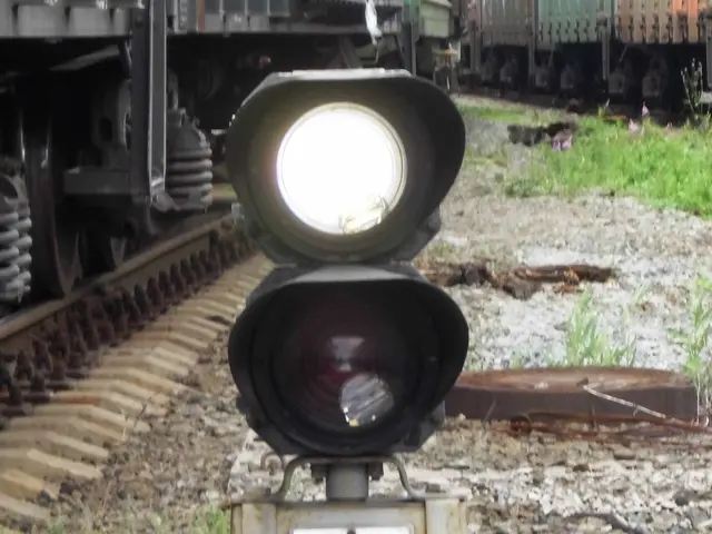 The image shows a railroad crossing signal with a train on the tracks in the background. The signal...
