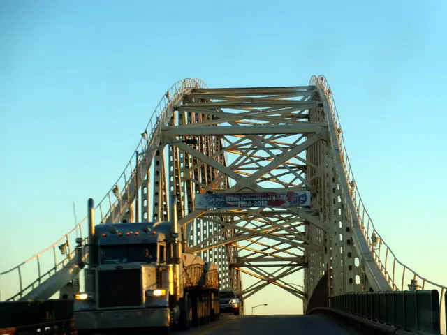 The image shows a semi truck driving across a bridge with railings on either side. There is a board...