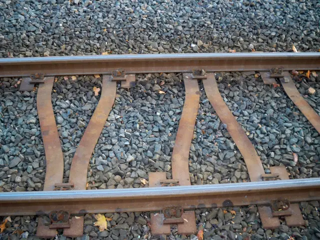 The image shows a close up of a train track with gravel on it. The track is composed of two railway...