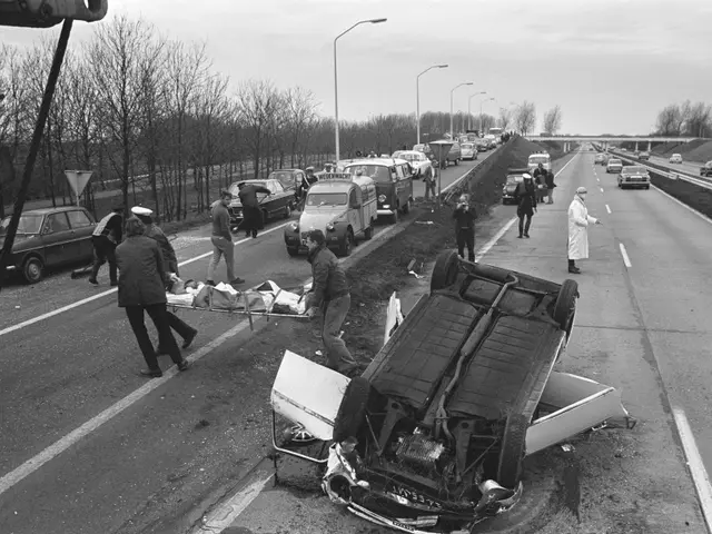 The image shows a black and white scene of a car that has been flipped over on the side of the...