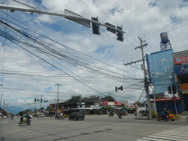 The image shows a city street filled with lots of traffic and power lines. There are vehicles on...
