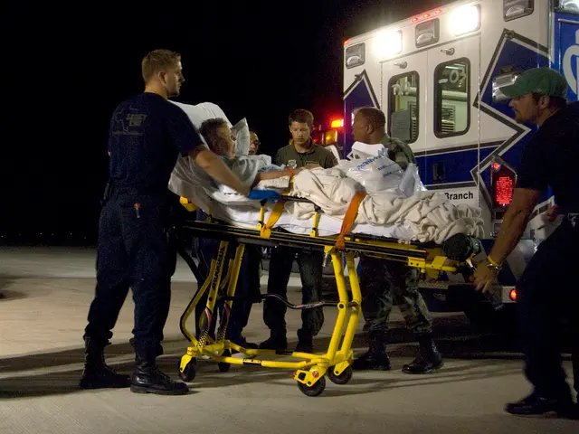 The image shows a man being loaded onto an ambulance by emergency personnel. He is lying on a...