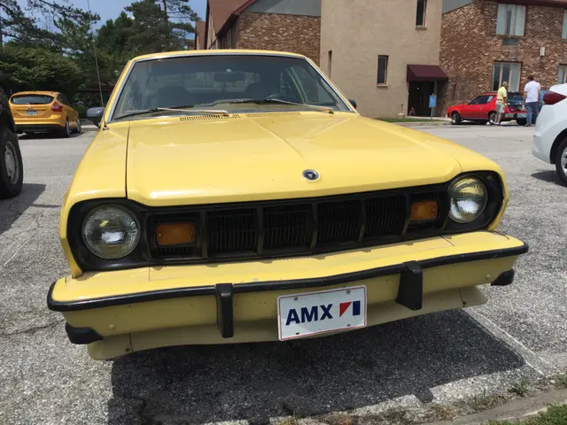The image shows a yellow BMW 2002 parked in a parking lot next to other cars, with people standing...