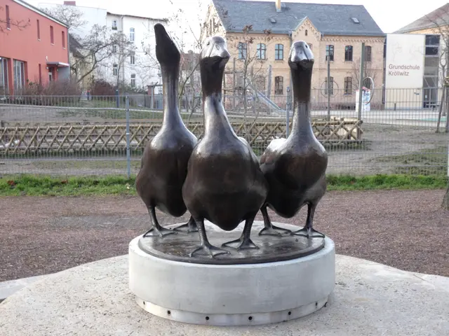 The image shows a bronze sculpture of three geese standing on top of a cement pedestal in the...