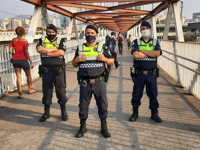 The image shows two police officers standing on a bridge with their arms crossed, surrounded by a...