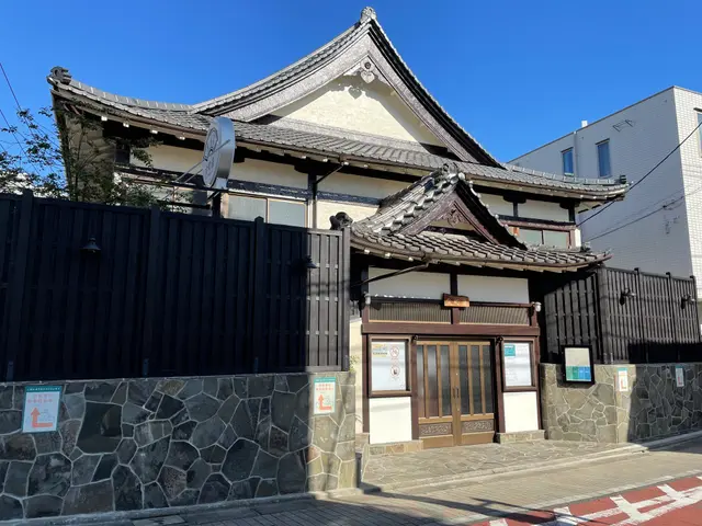 The image shows a traditional Japanese building with a black fence in front of it, surrounded by...