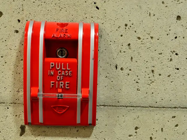 The image shows a red fire alarm mounted on the side of a building. It is a cylindrical box with a...