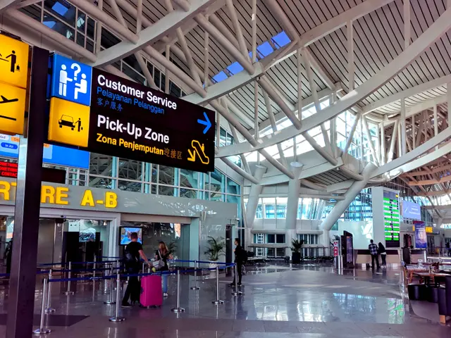The image shows an inside view of an airport terminal with people walking through it. There are...