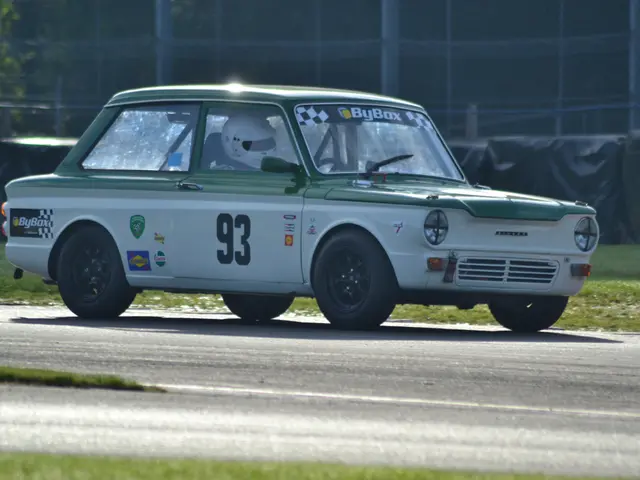 The image shows a green and white car driving down a race track, with a person wearing a helmet...