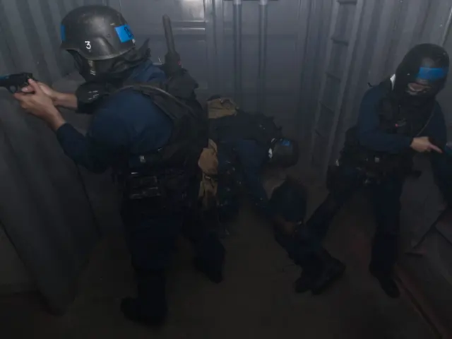 The image shows a group of police officers in riot gear standing next to each other, with one of...