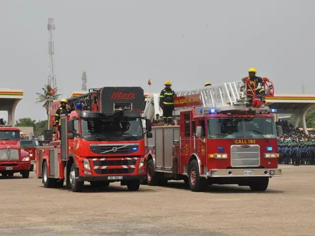 The image shows a group of fire trucks parked next to each other in a parking lot. There are people...
