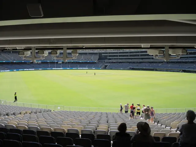 The image shows a large stadium filled with lots of people watching a game of cricket. There are...