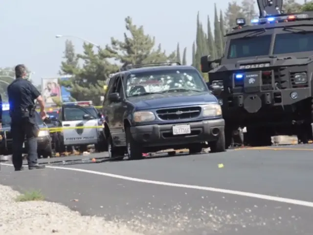 The image shows a police car parked on the side of the road next to a police truck, with a group of...