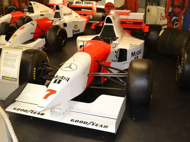 The image shows a group of race cars on display in a museum, with people standing around them....