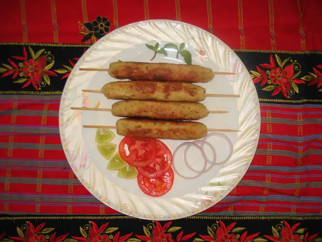 The image shows a plate with three kebabs on skewers, accompanied by slices of tomato and onions....