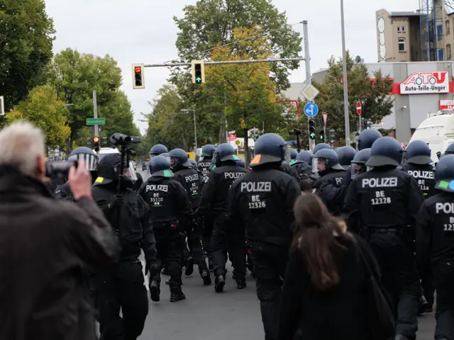 The image shows a group of police officers walking down a street next to a crowd. They are wearing...