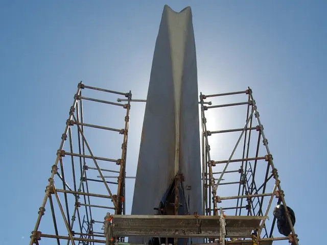 The image shows a large boat being built in a shipyard, with scaffolding surrounding it. The sky is...