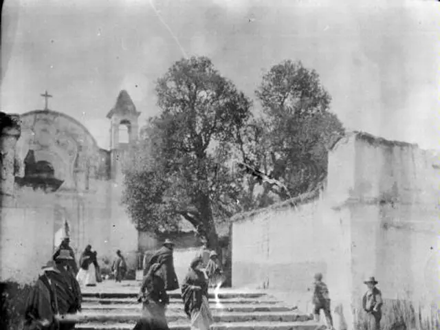 The image shows a group of people walking down a street in front of a church, with steps leading up...