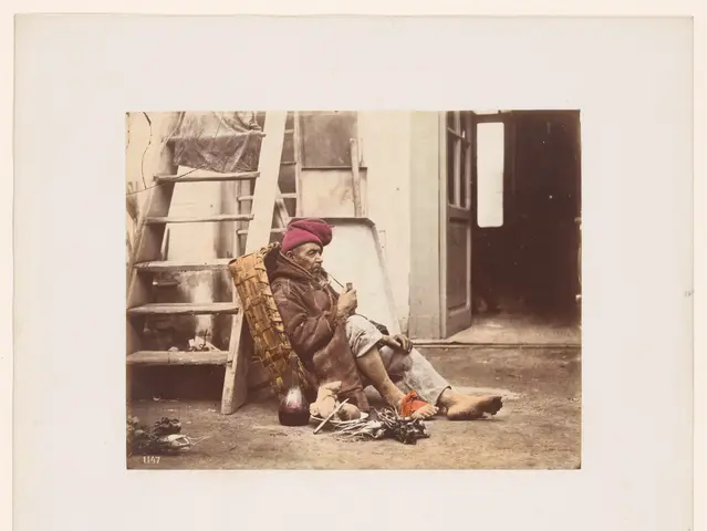 The image shows an old man sitting on the ground next to a ladder, wearing a cap and holding...