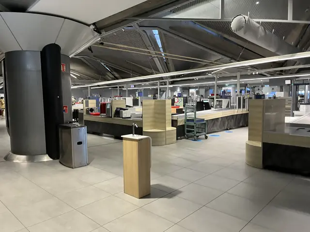 The image shows a large room filled with lots of tables and chairs, dustbins, machines, pillars,...