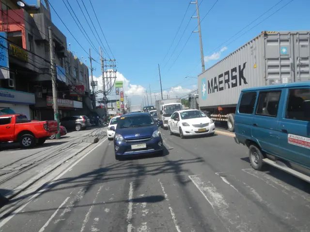 The image shows a city street filled with lots of cars and trucks, including a van and a pickup...