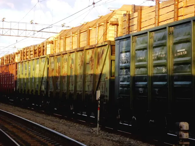The image shows a freight train traveling down train tracks, surrounded by a forest of trees and a...