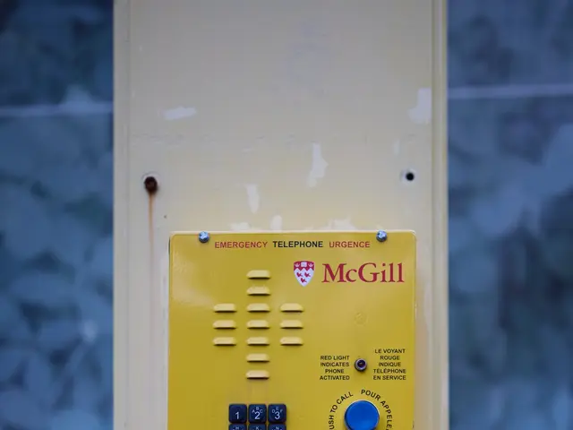 The image shows a yellow emergency phone mounted on the side of a building, with a wall in the...