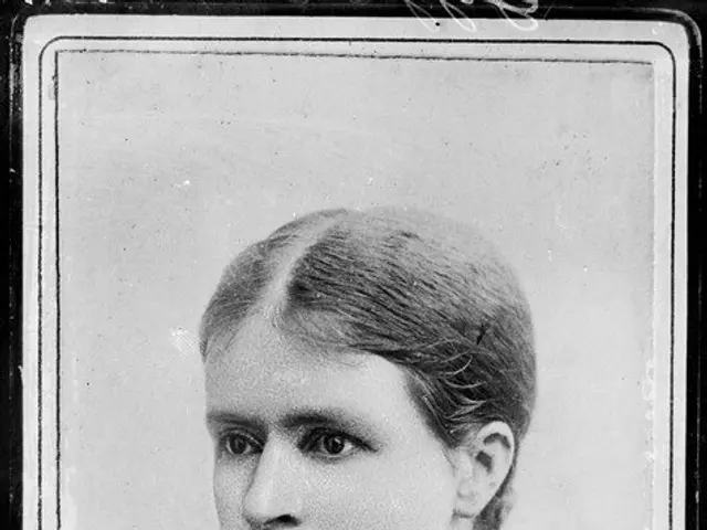 The image shows an old black and white photo of a woman wearing a necklace. At the bottom of the...