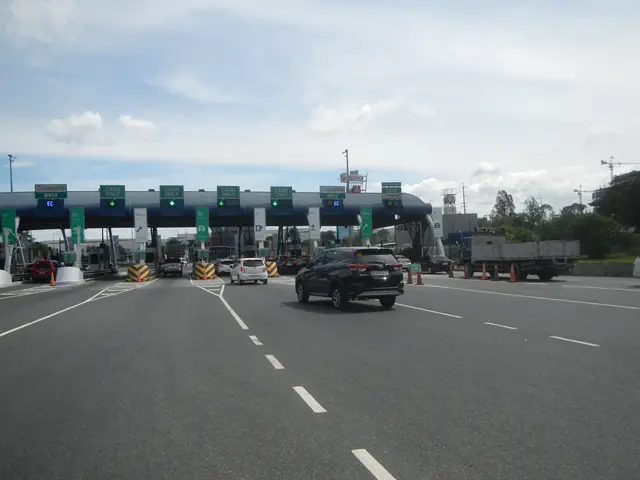 The image shows a highway with cars driving down it and a toll booth in the background. There are...