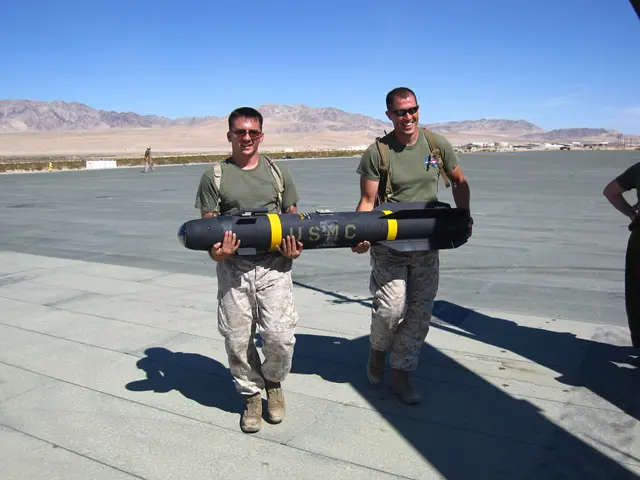 The image shows two men in military uniforms carrying a large bomb on top of an airport tarmac....