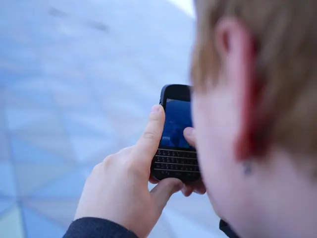 In this image a person is holding a mobile phone. He is on a street.