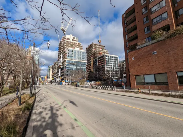 The image shows a city street with tall buildings in the background, street poles, street lights,...