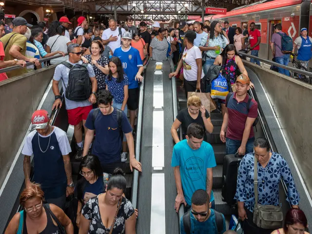 The image shows a group of people standing on top of an escalator in a train station, with a train...