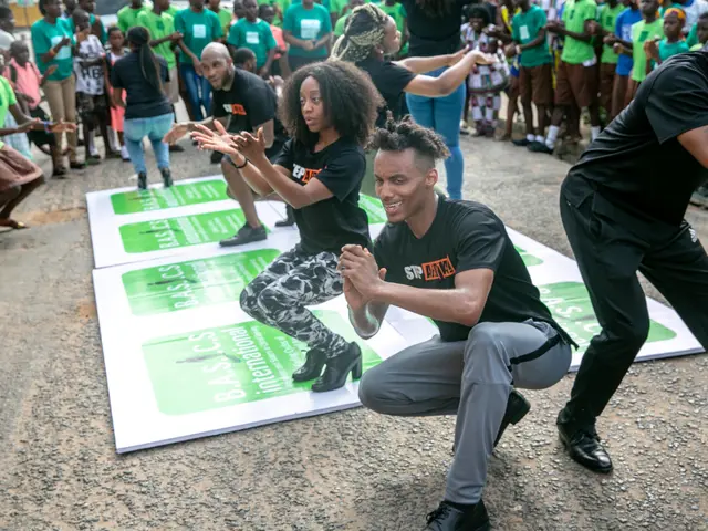 The image shows a group of people in green shirts and black pants dancing on a stage in front of a...